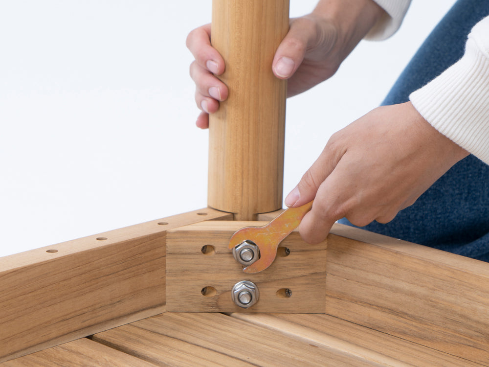 A person assembling a Neighbor teak outdoor dining table leg